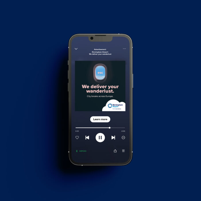 Iphone on a blue background playing a Spotify ad. Text reads 'we deliver your Wanderlust. City breaks across Europe. Birmingham Airport'